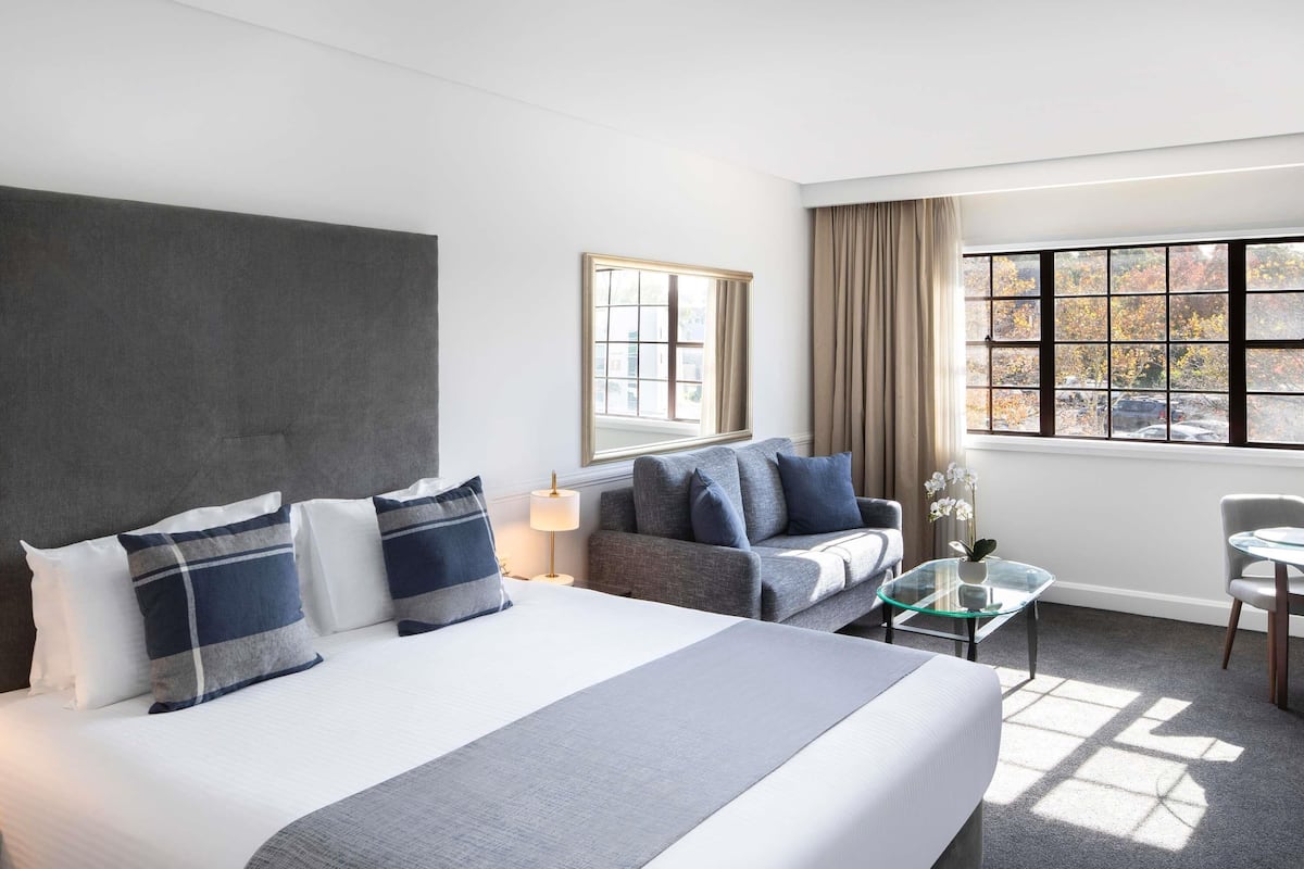 Ein Hotelzimmer mit Bett, einer Couch, einem kleinen Tisch und einem Fenster mit Vorhängen.