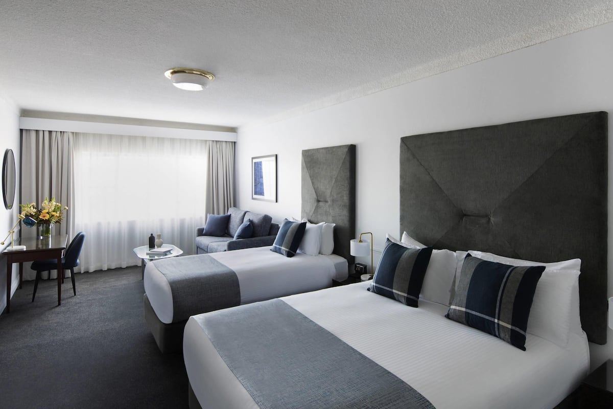 Ein Hotelzimmer mit zwei Betten, einem Schreibtisch, einem Stuhl, einer Lampe und einer Blumenvase.