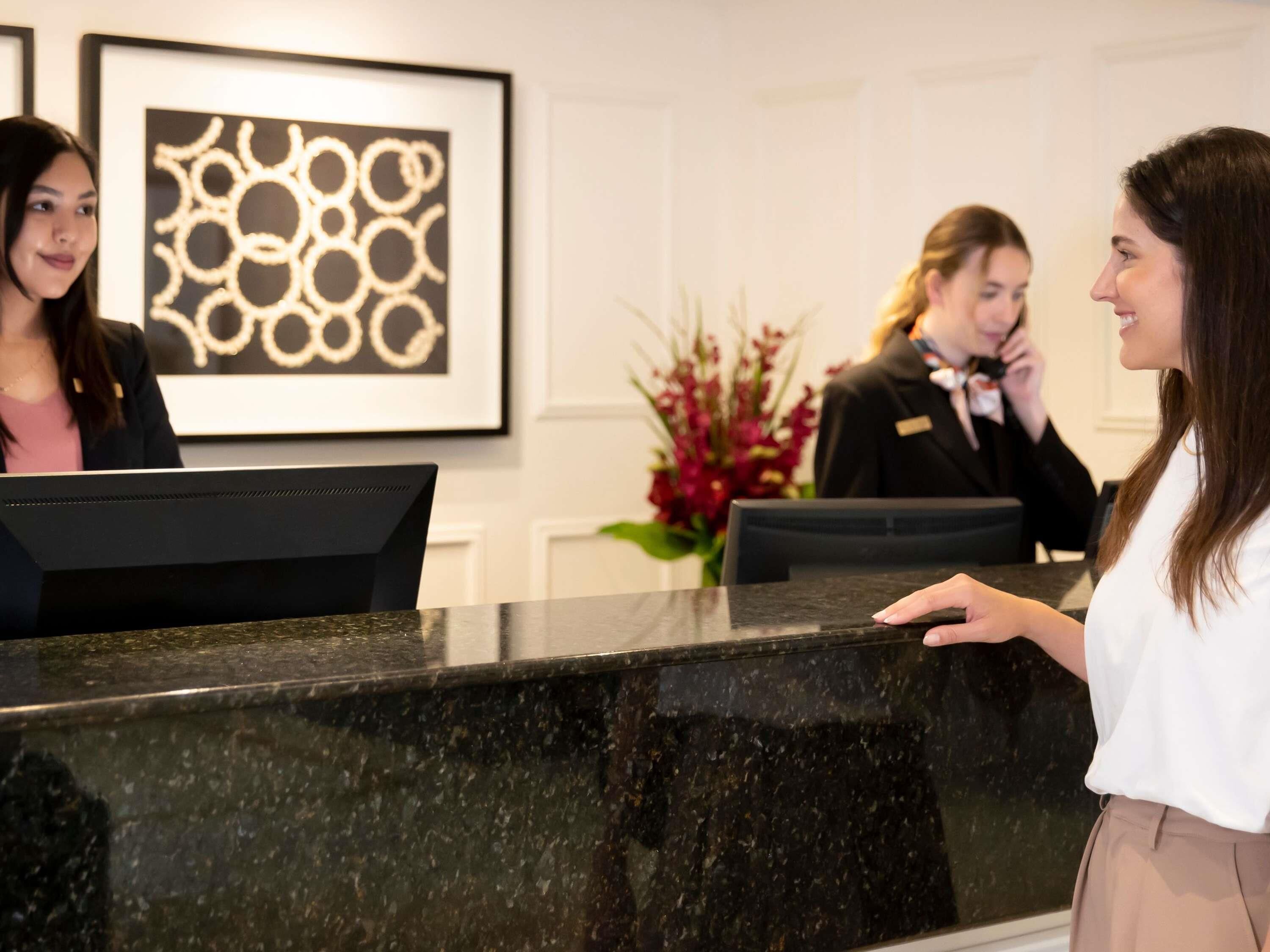 A reception desk with a black marble top, framed artwork on the wall, and a floral arrangement in the background.