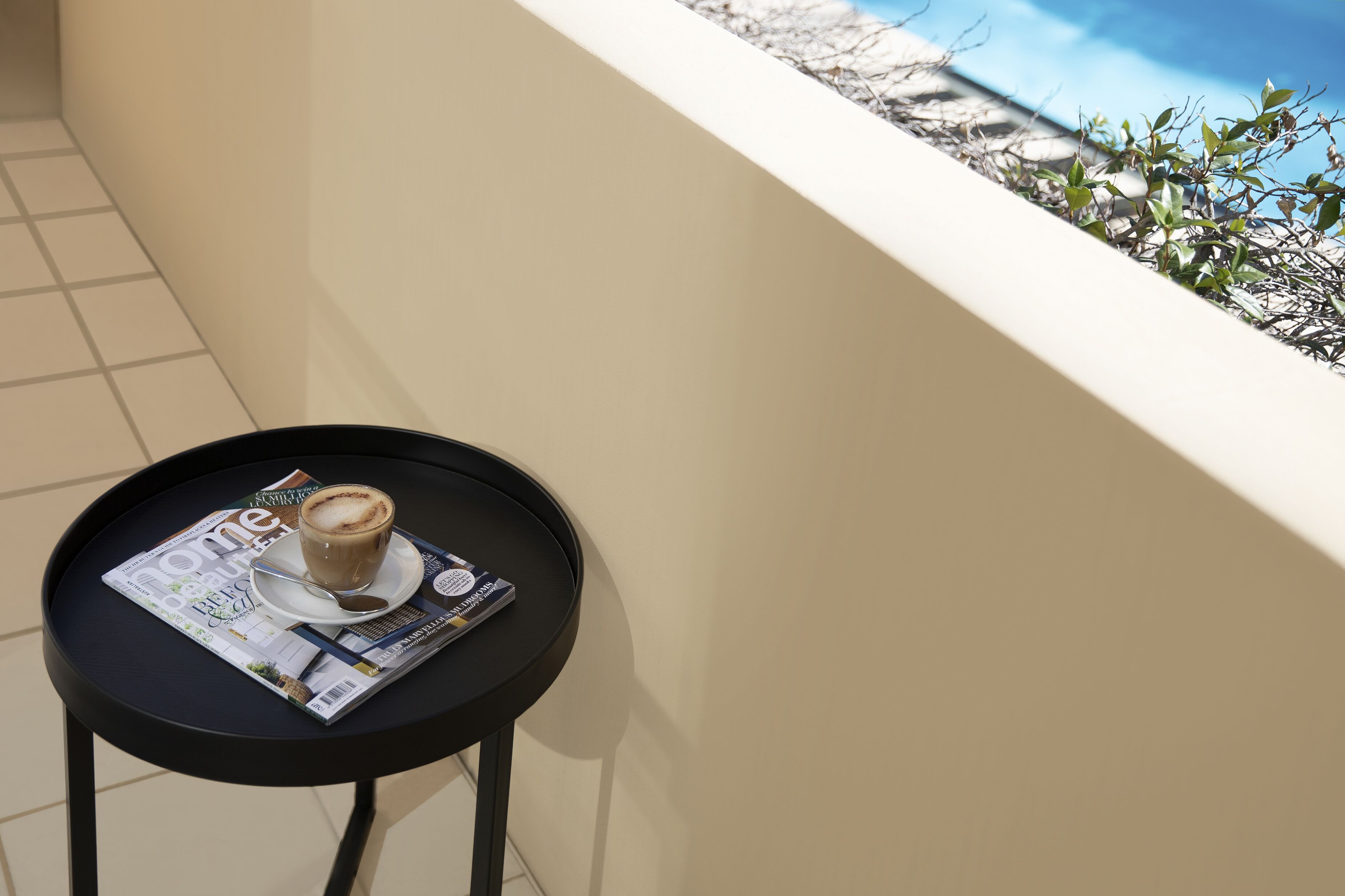 A small round table with a magazine, a cup of coffee, and a pair of sunglasses.