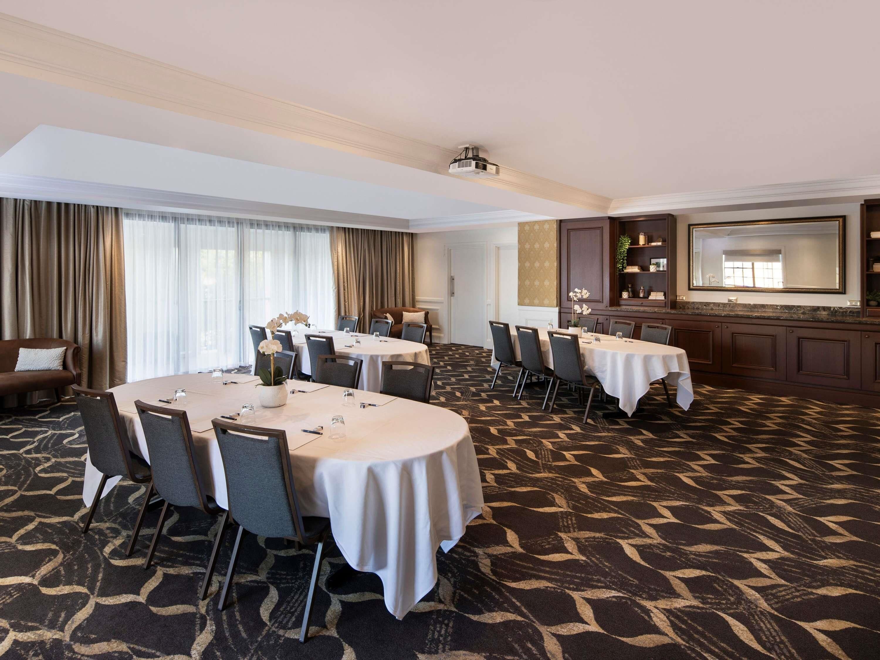 A conference room with multiple tables, chairs, a projector, and a large mirror.