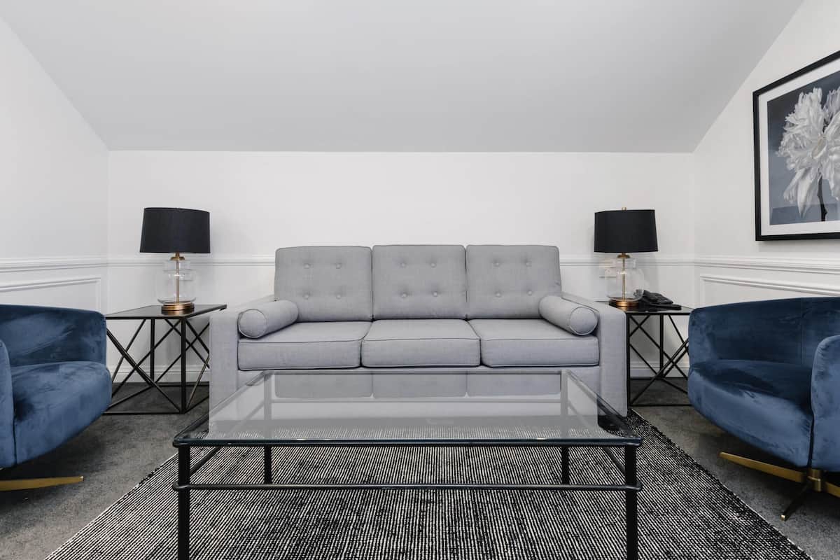 Ein modernes Wohnzimmer mit einem grauen Sofa, zwei Beistelltischen mit Lampen, einem Glastisch und einem schwarz-weißen Teppich.