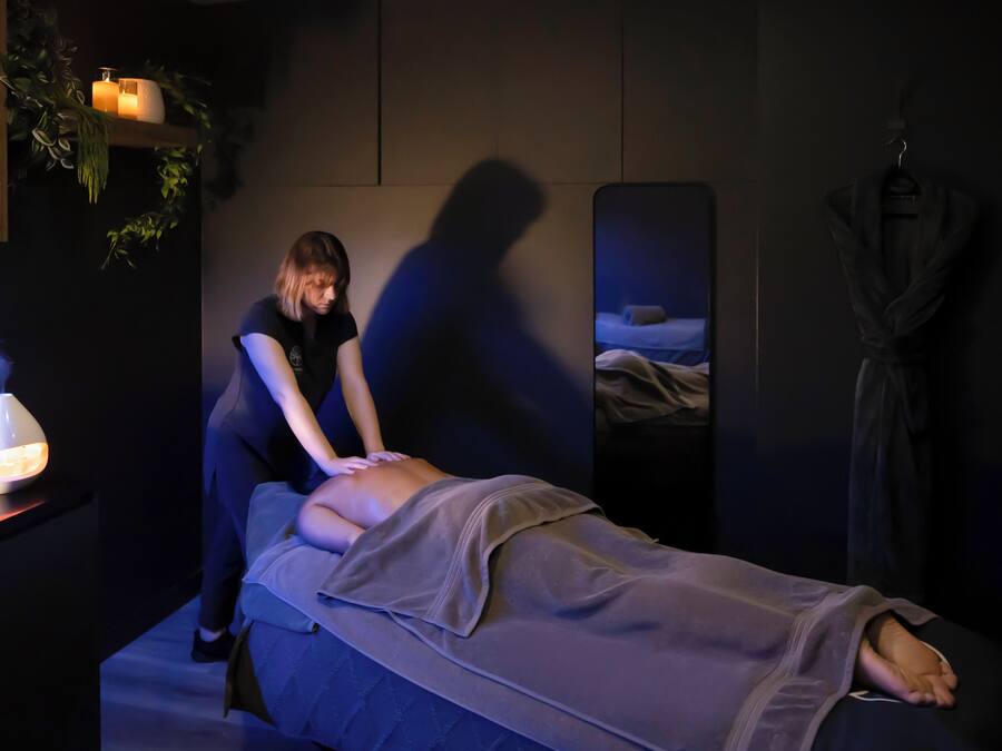 A massage therapy room with a massage table, a massage therapist, a lit lamp, and a robe hanging on the wall.
