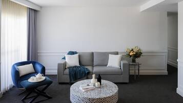 A modern living room with a grey sofa, a blue armchair, a round coffee table, and a small side table with a vase of flowers.