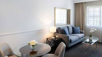 Hotellihuone, jossa on sohva, lasinen sohvapöytä, pyöreä pöytä ja lamppu.