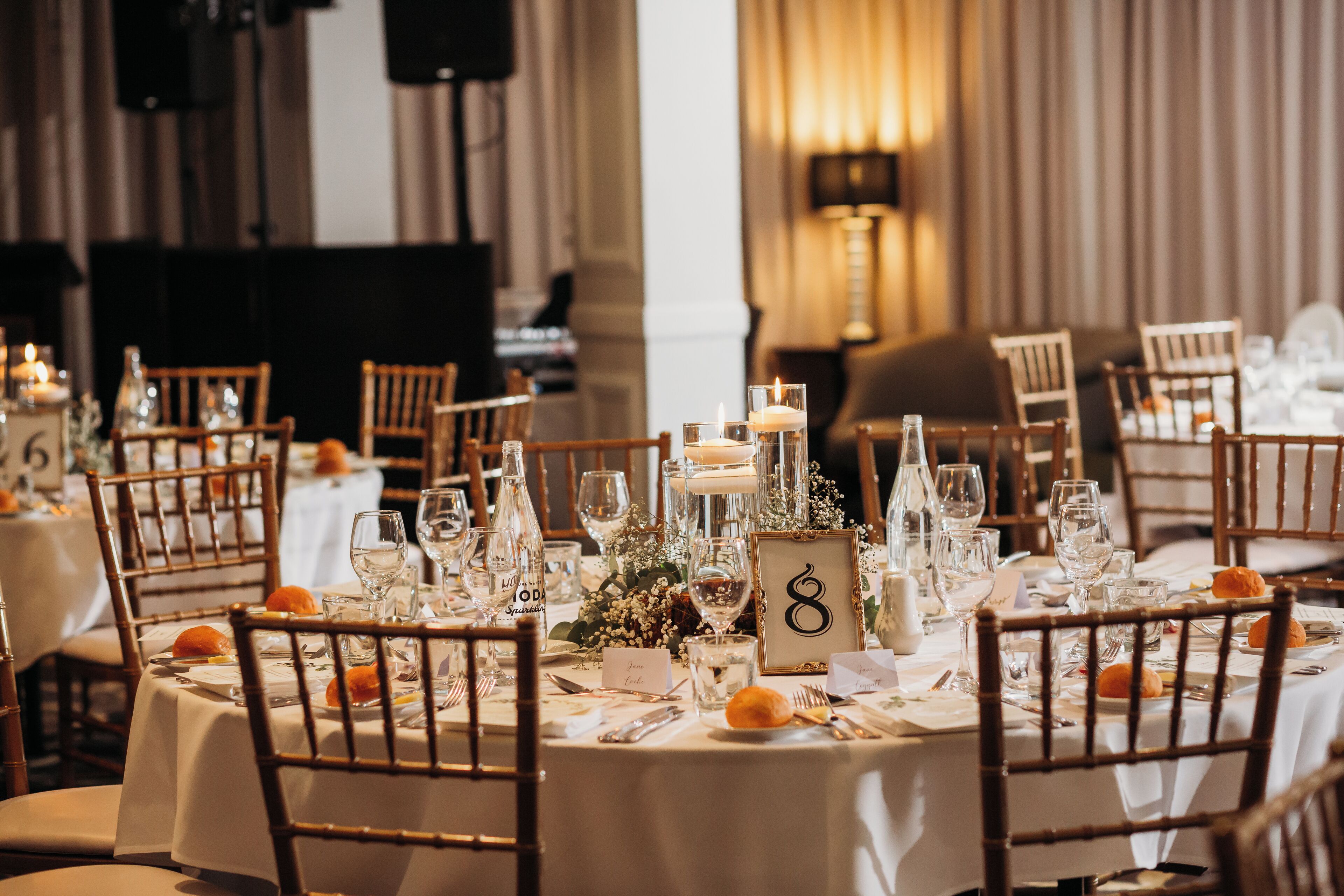 A dining area with round tables, wooden chairs, and white tablecloths.