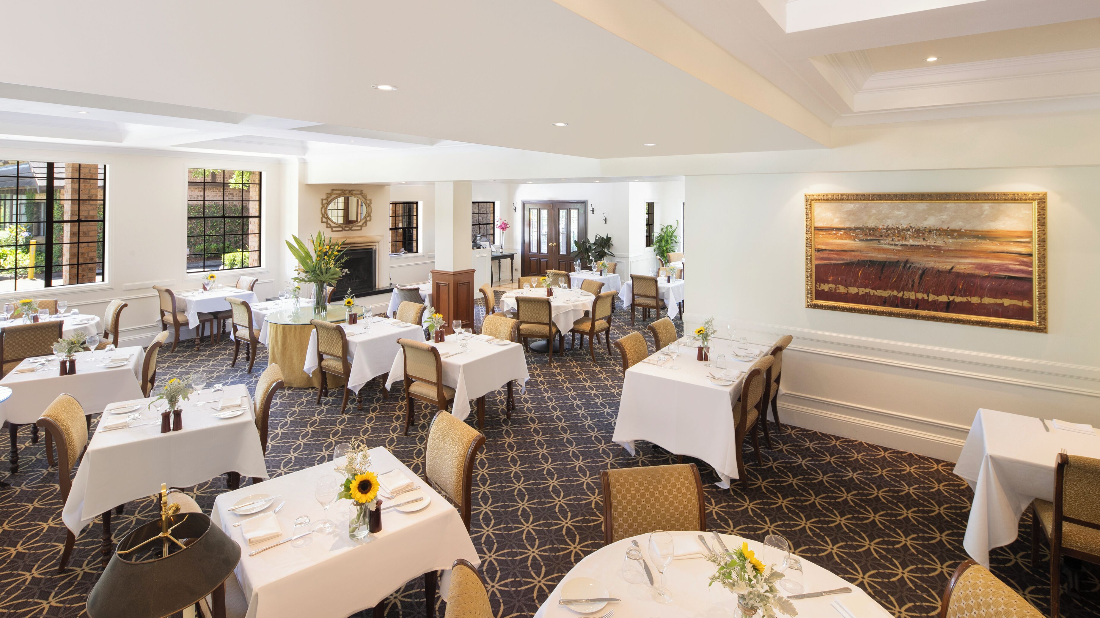 A spacious dining area with multiple tables set for guests, featuring a patterned carpet and elegant decor.