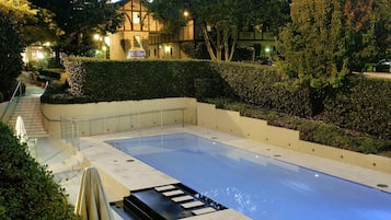 En rektangulär swimmingpool med ett svart område för avkoppling i bubbelbad, omgiven av välskötta häckar och träd.