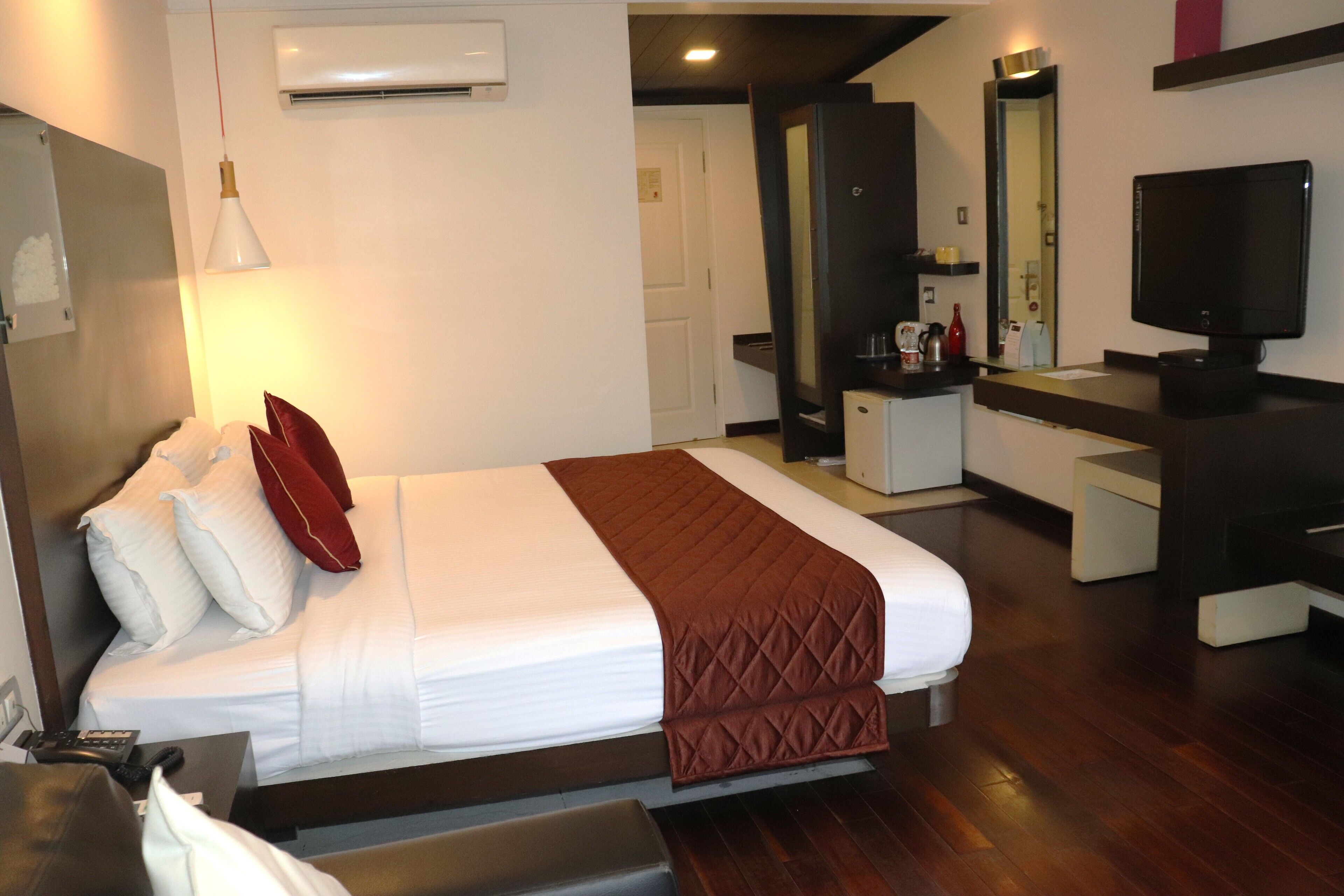 Habitación de hotel con cama, mesita de noche, televisor y escritorio con espejo.