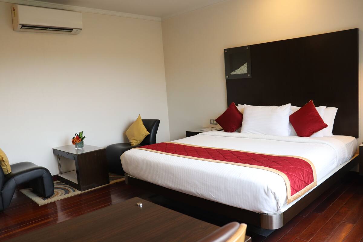 A hotel room with a large bed, a bedside table, a chair, and a desk.