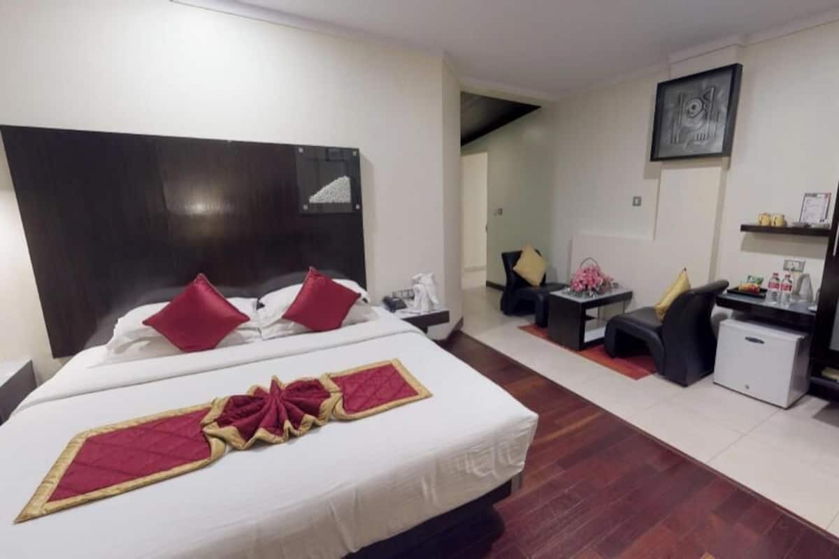 A hotel room with a large bed, a desk, a chair, a small table, and a wardrobe.