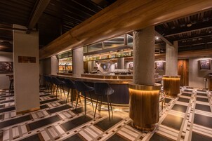 A bar area with a modern design, featuring a bar counter, stools, and a patterned floor.