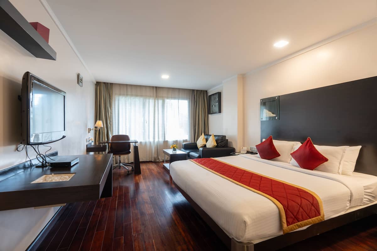 A hotel room with a large bed, a desk, a TV, and a seating area.