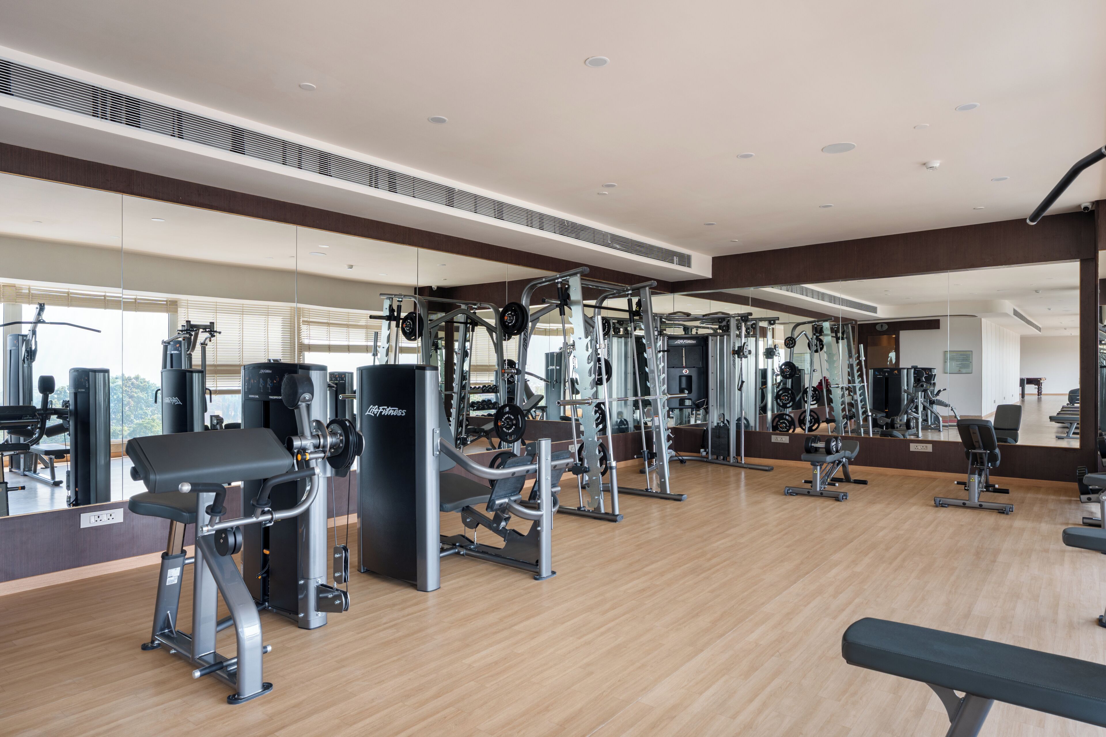 Une salle de sport moderne équipée de divers appareils d’exercice, de grands miroirs et d’un plancher en bois.