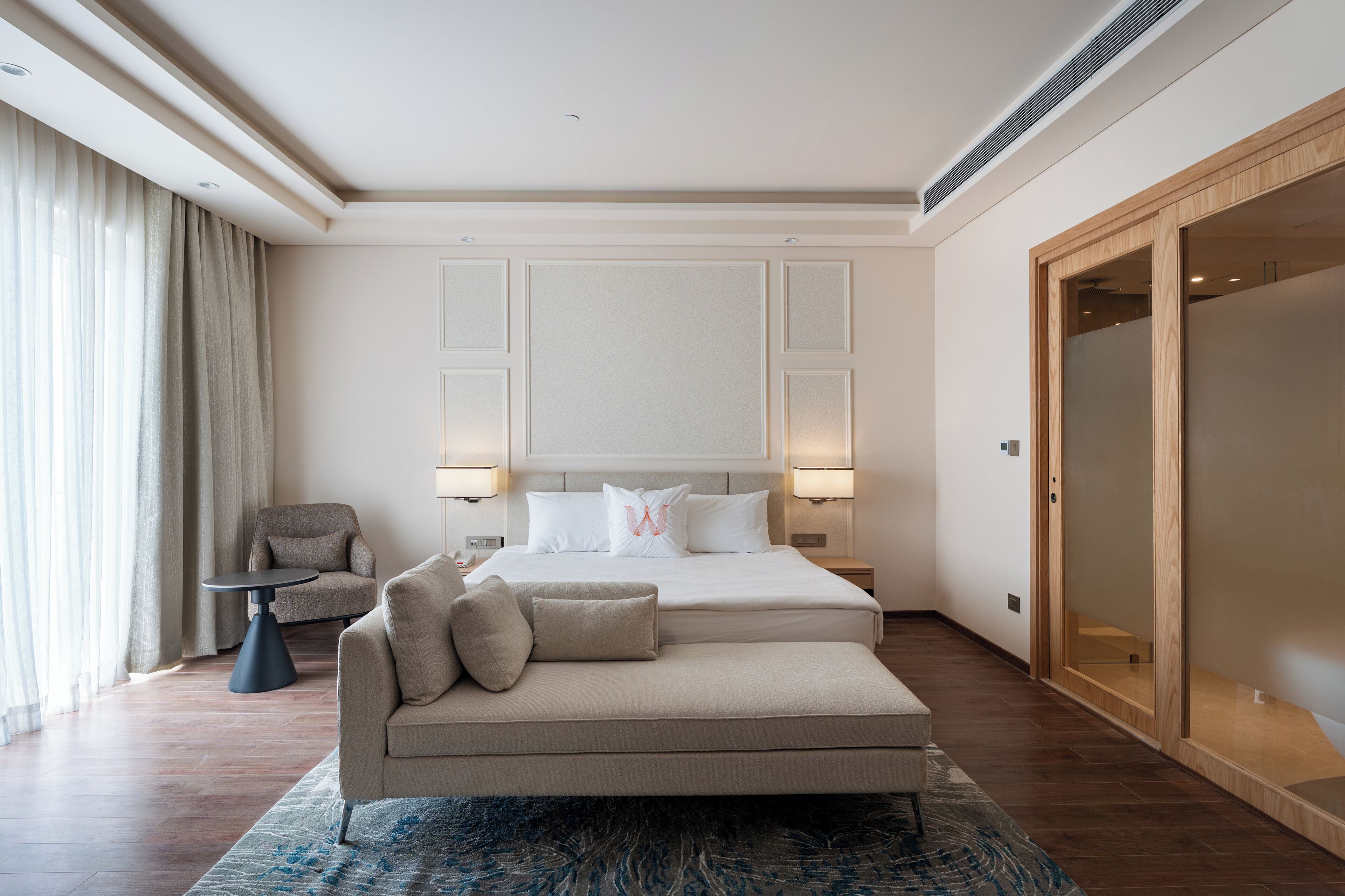 A modern hotel room with a large bed, a sofa, a small table, and a wardrobe.