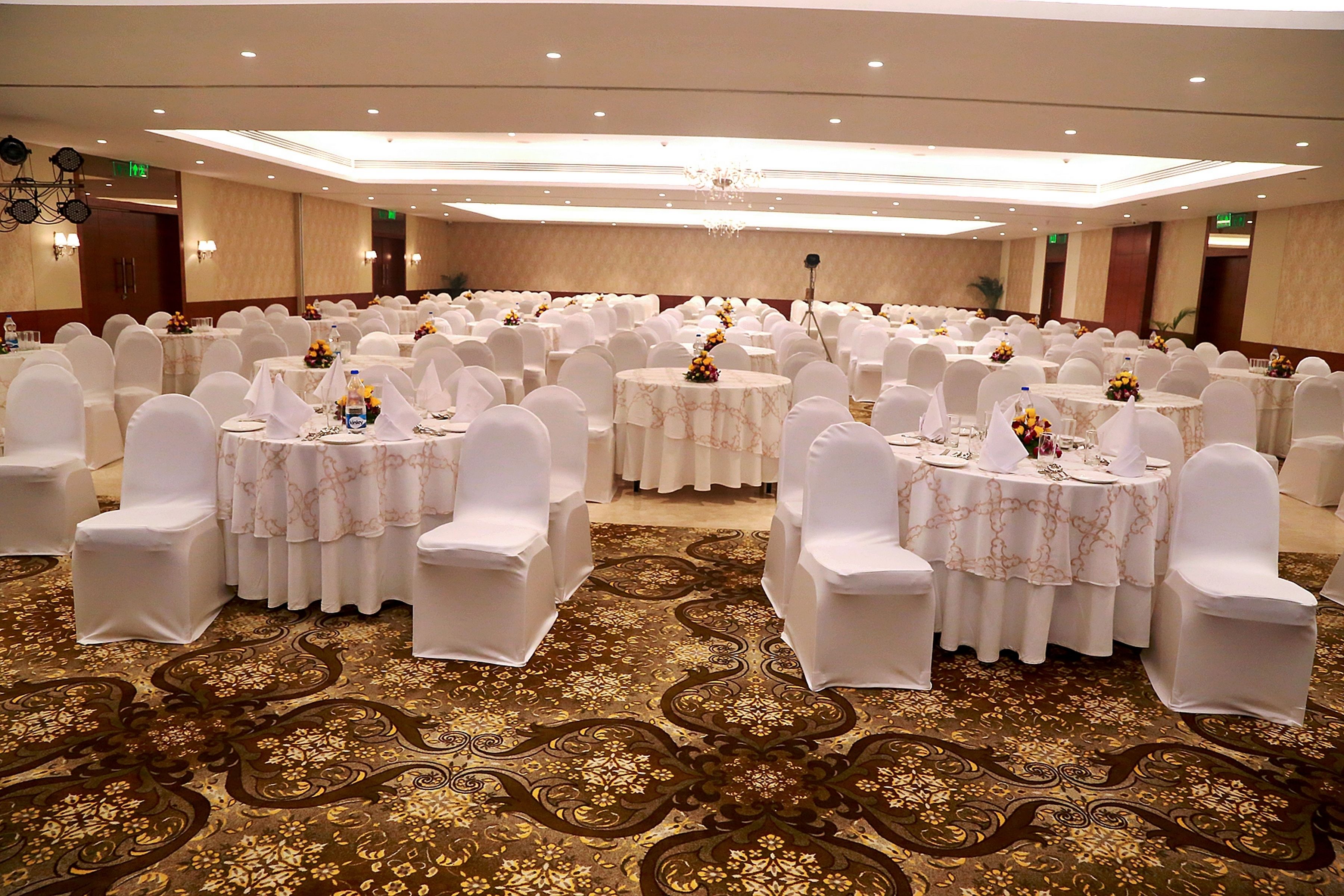 A banquet hall with round tables, white chairs, and floral centerpieces.
