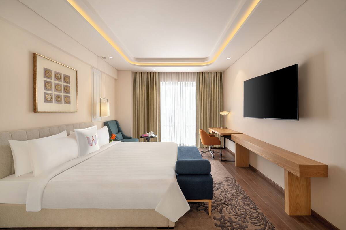 Ein Hotelzimmer mit einem großen Bett, einem Schreibtisch, einem Sessel, einem Fernseher und einem gerahmten Kunstwerk an der Wand.