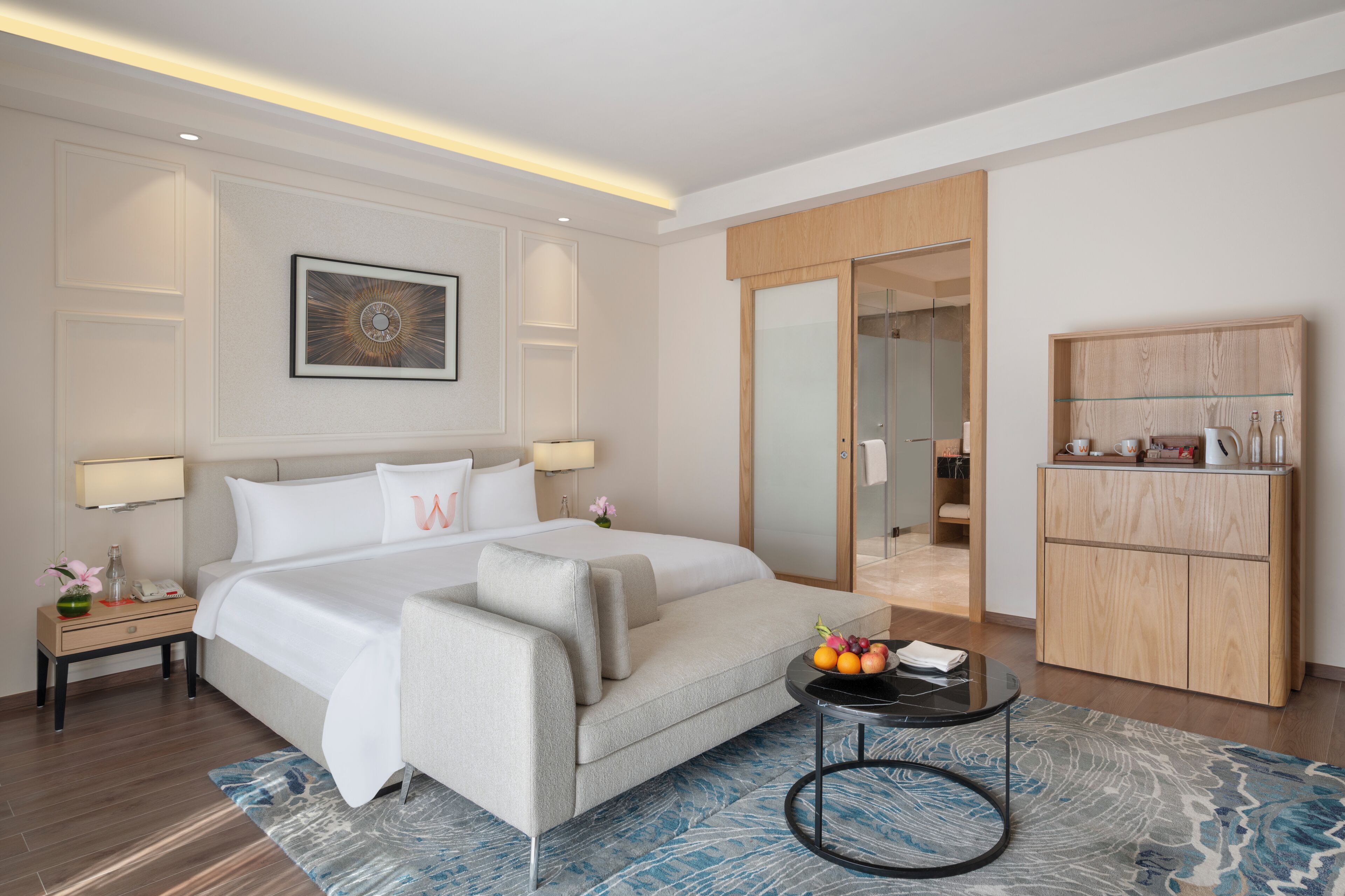 A modern hotel room with a large bed, bedside tables, a round coffee table, and a wardrobe.