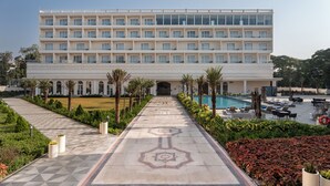Un hôtel à la façade symétrique, doté d’une entrée centrale et d’un espace piscine agrémenté de chaises longues et de parasols.