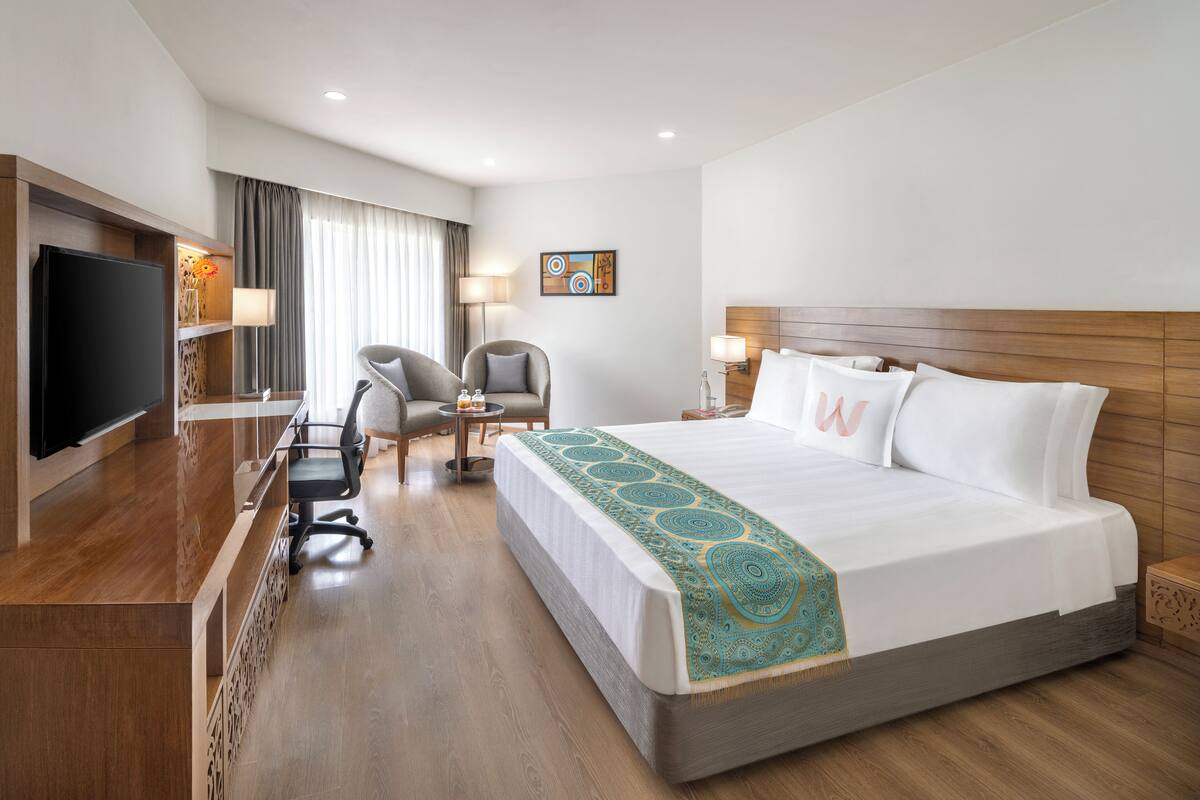 Ein Hotelzimmer mit einem großen Bett, einem Schreibtisch mit Flachbildfernseher, einem Sessel und einem kleinen Tisch.