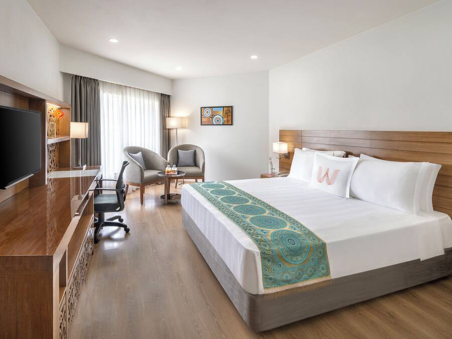 Une chambre d’hôtel avec un grand lit, un bureau doté d’un téléviseur à écran plat, une chaise et une petite table.