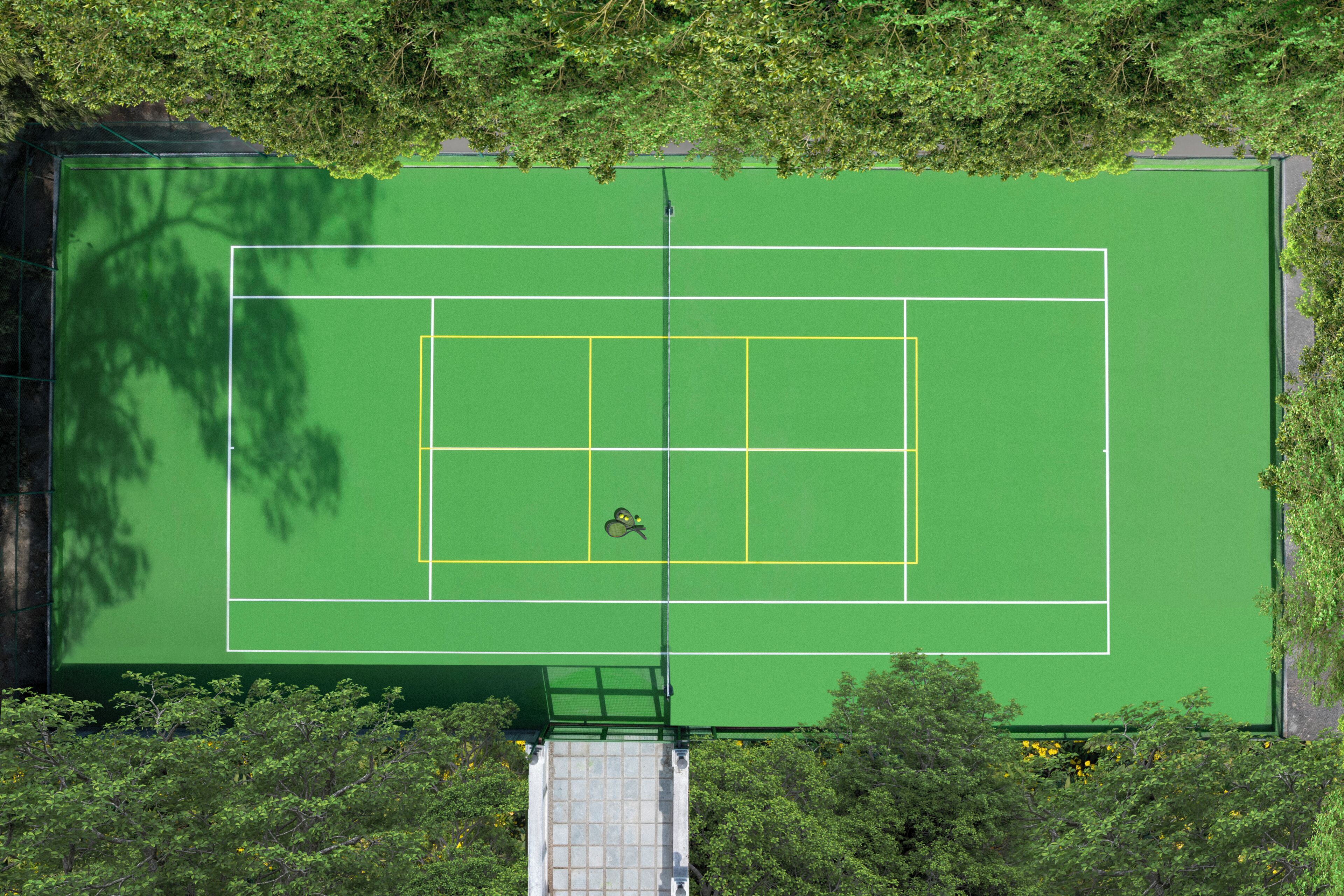 Vista aérea de una cancha de tenis rodeada de árboles.