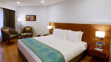 Una habitación de hotel con una cama grande, dos sillones, una mesita de noche con lámpara y una obra de arte en la pared.