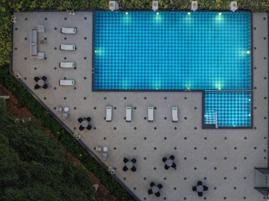 Vista aérea de una zona de piscina en la azotea, con varias tumbonas, sillones y mesas.