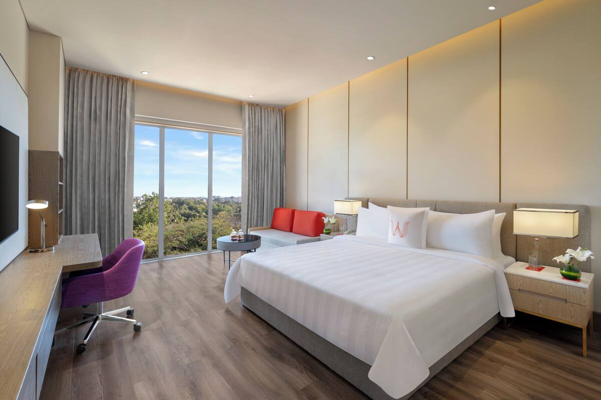 Ein Hotelzimmer mit einem großen Bett, einem Schreibtisch mit Stuhl, einem Fernseher und Blick ins Freie.