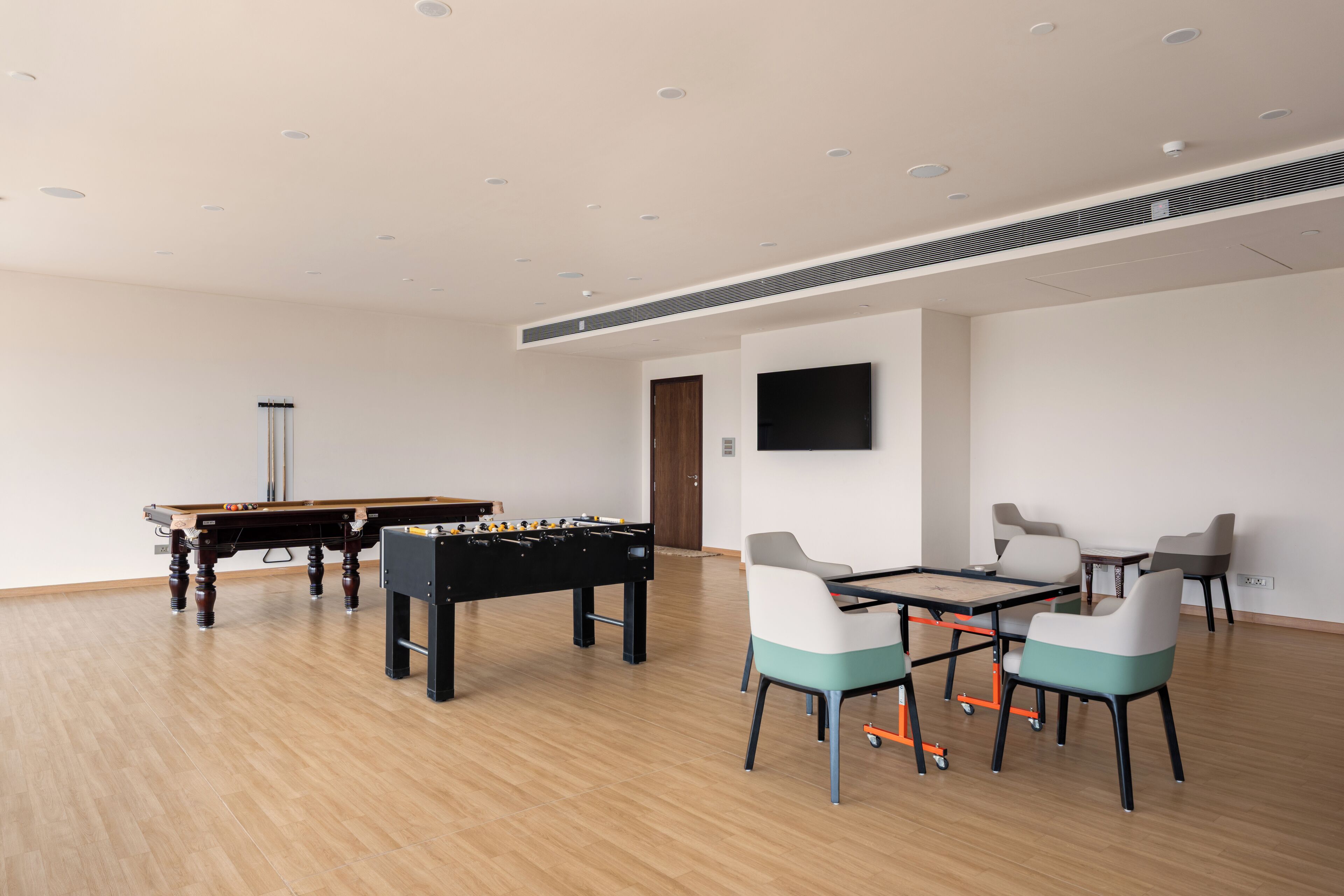 A room with a foosball table, a pool table, and a TV mounted on the wall.