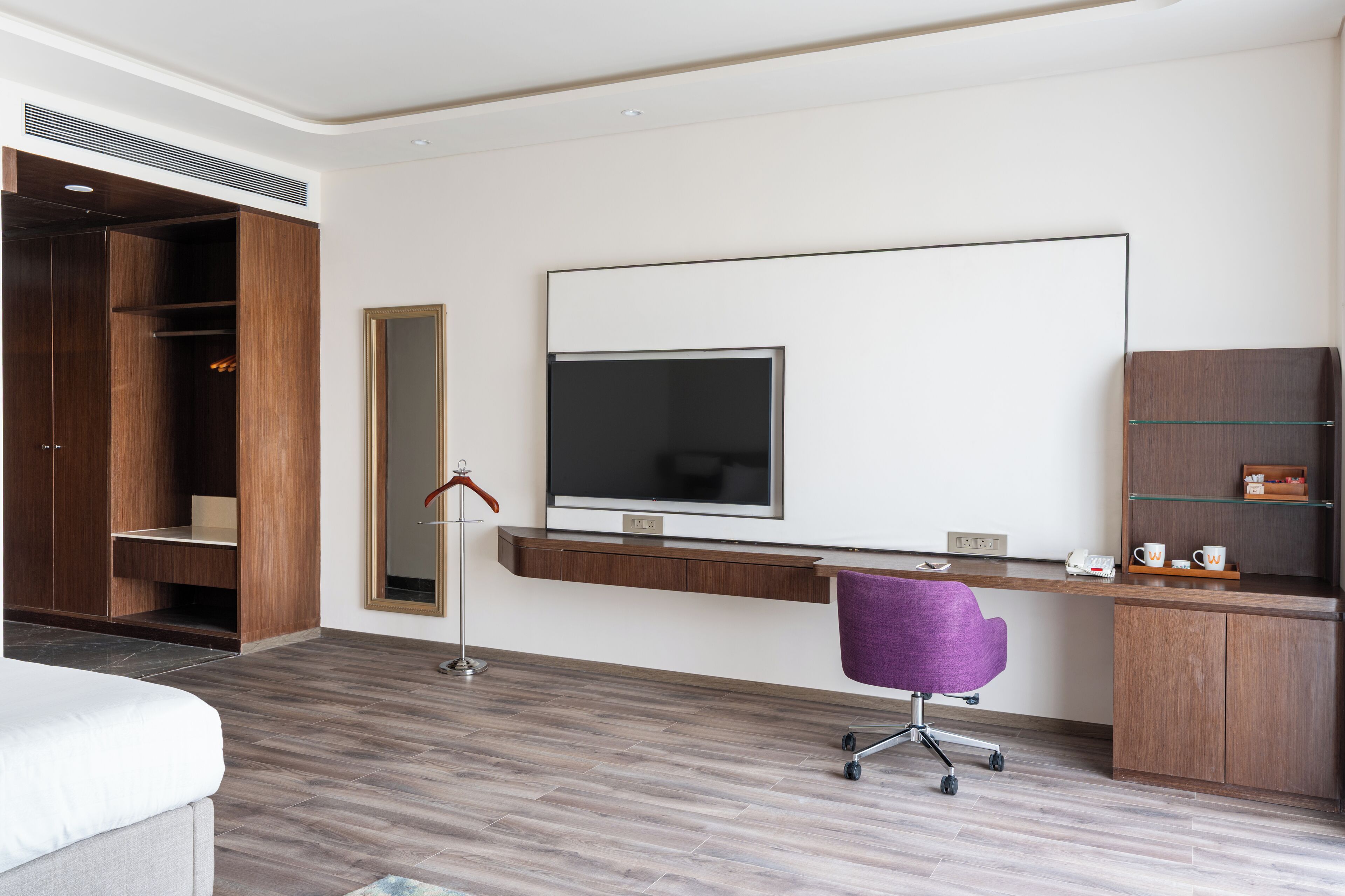 A modern hotel room with a large bed, a desk with a computer, a TV, and a wardrobe.