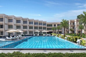 Ein Swimmingpool mit Liegestühlen und Sonnenschirmen, umgeben von einem mehrstöckigen Hotelgebäude mit Balkonen.