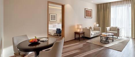 A hotel room with a dining area, a living room, a bed with a view, and a chandelier.