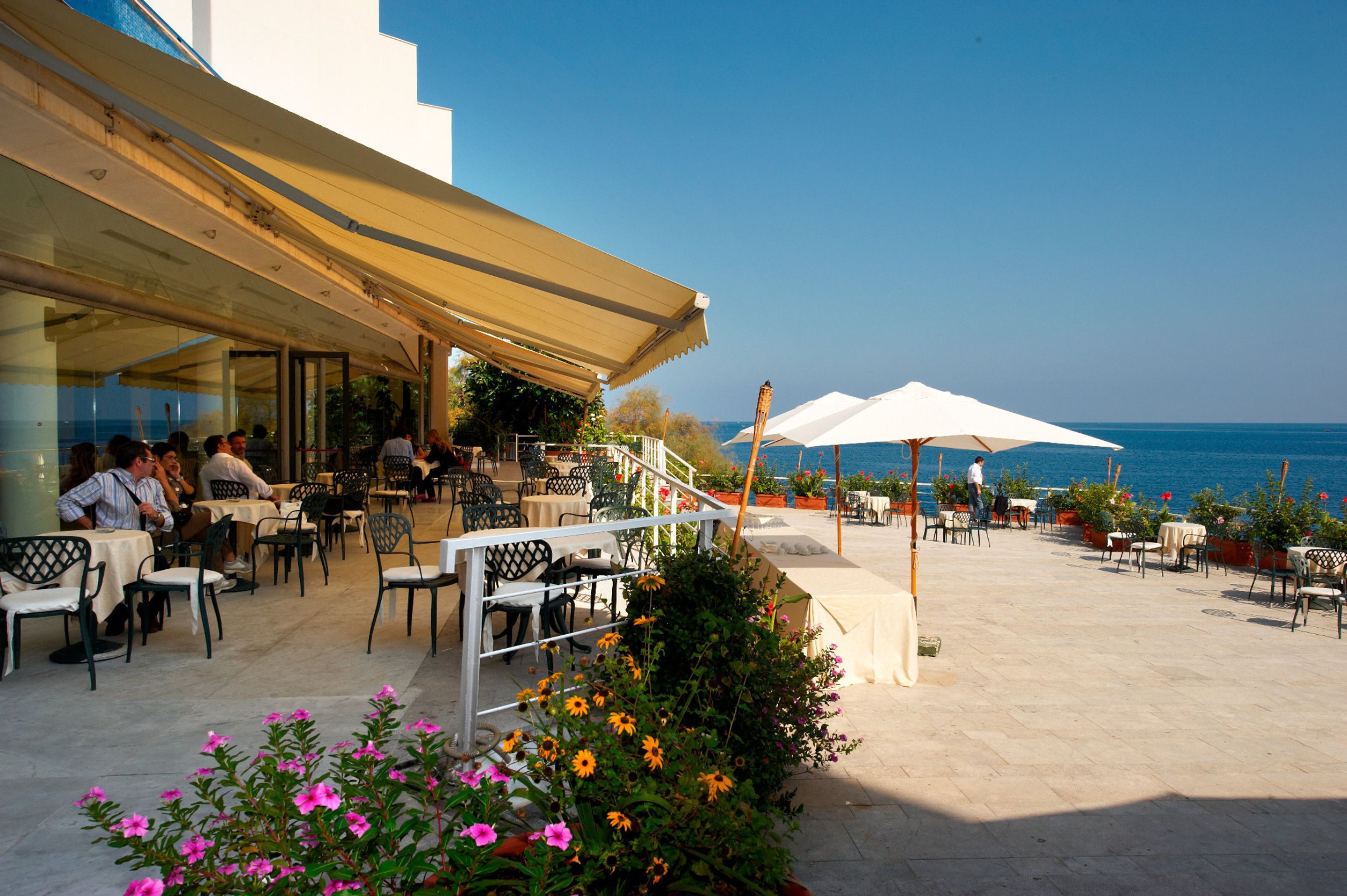 Un espace extérieur aménagé avec des tables et des chaises, une allée couverte et une vue sur la mer.