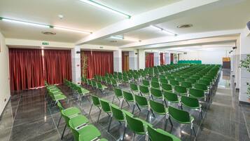 A conference room with rows of green chairs, a stage with a red curtain, and a green exit sign.
