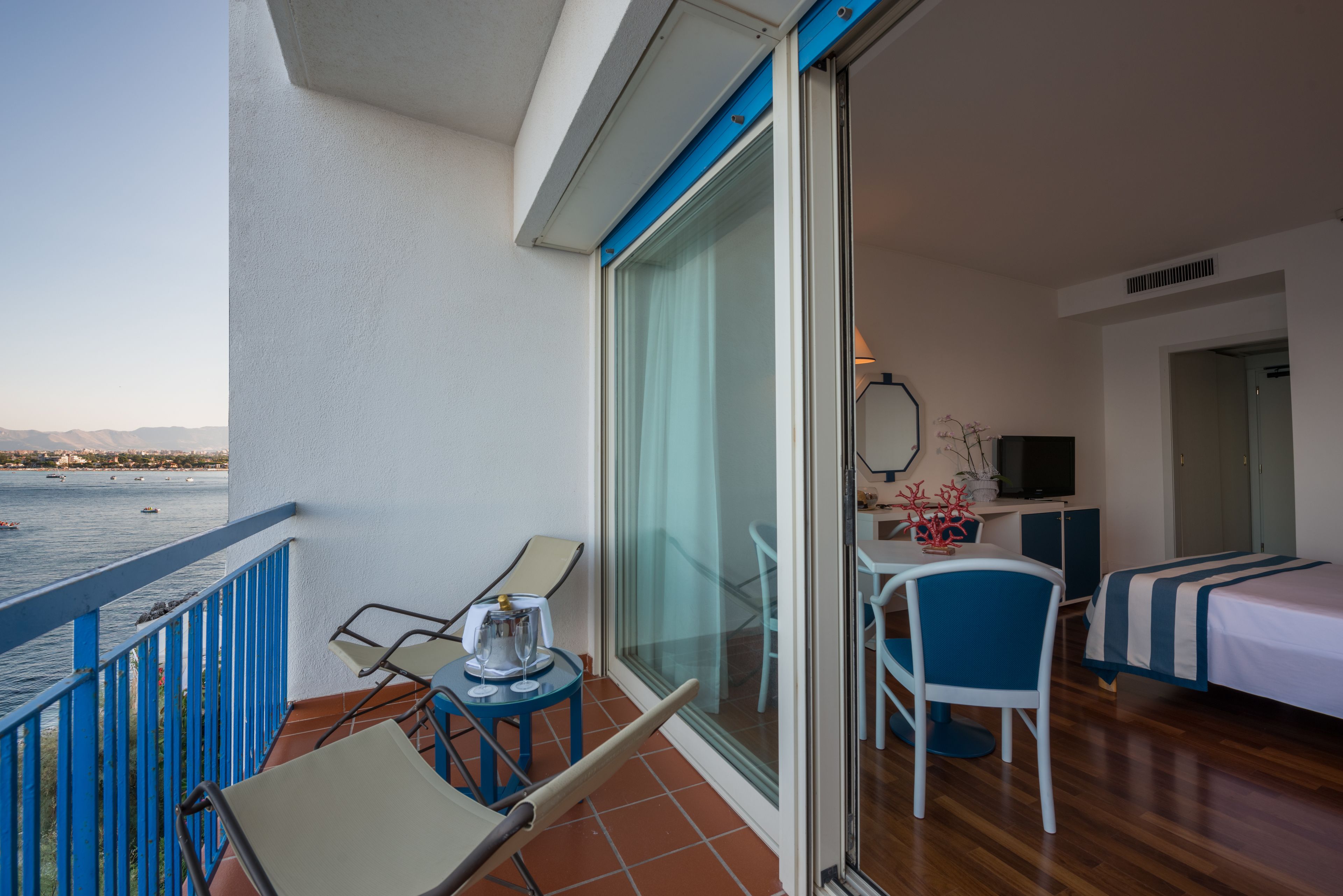 Un balcón con vista al mar, una mesa con sillas, una cama y un televisor.