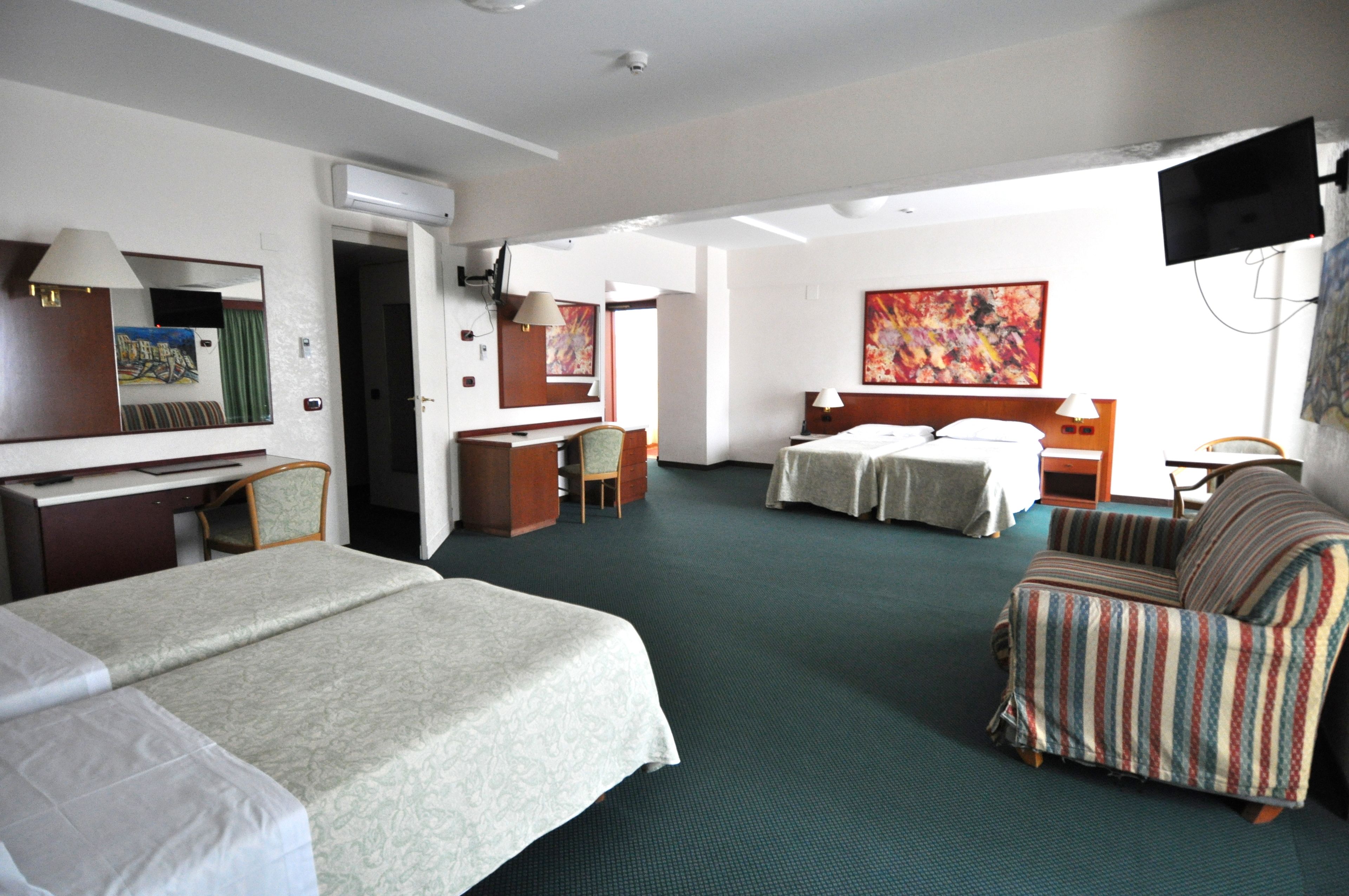Habitación de hotel con dos camas, un sofá, un escritorio y una televisión.