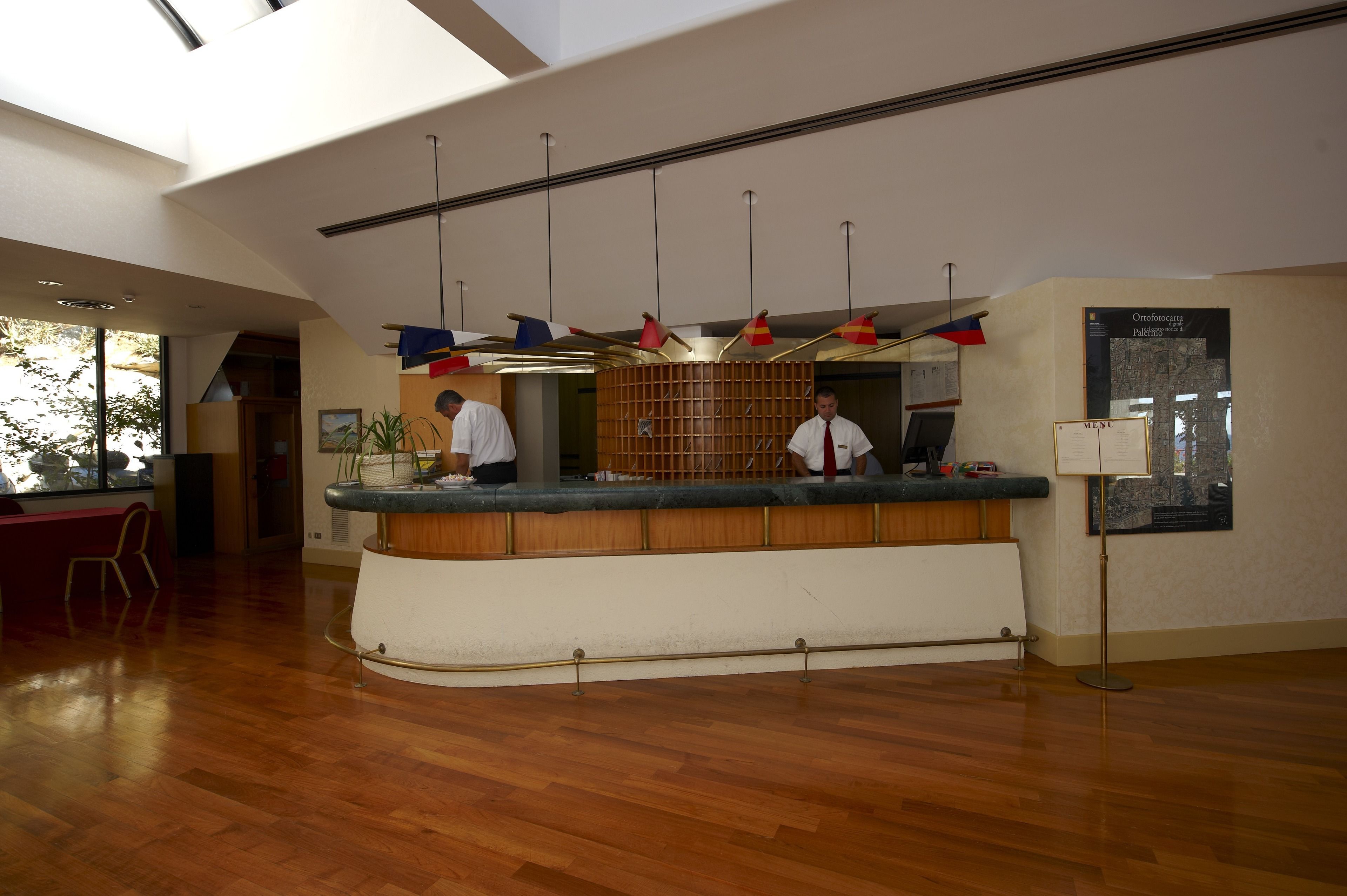 A reception area with a wooden counter, two staff members, and a menu stand.