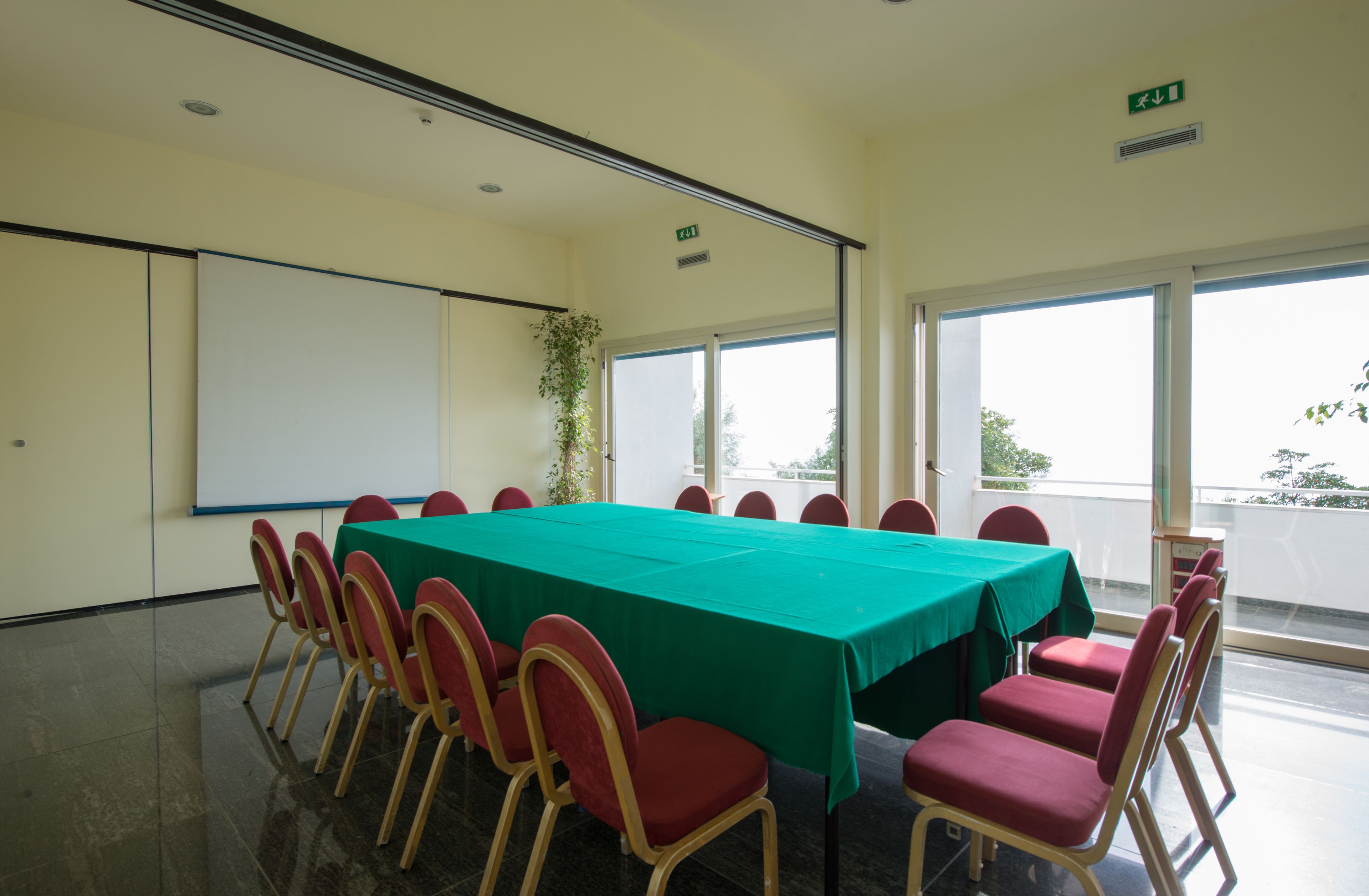 A conference room with a long table, red chairs, a projector screen, and large windows.