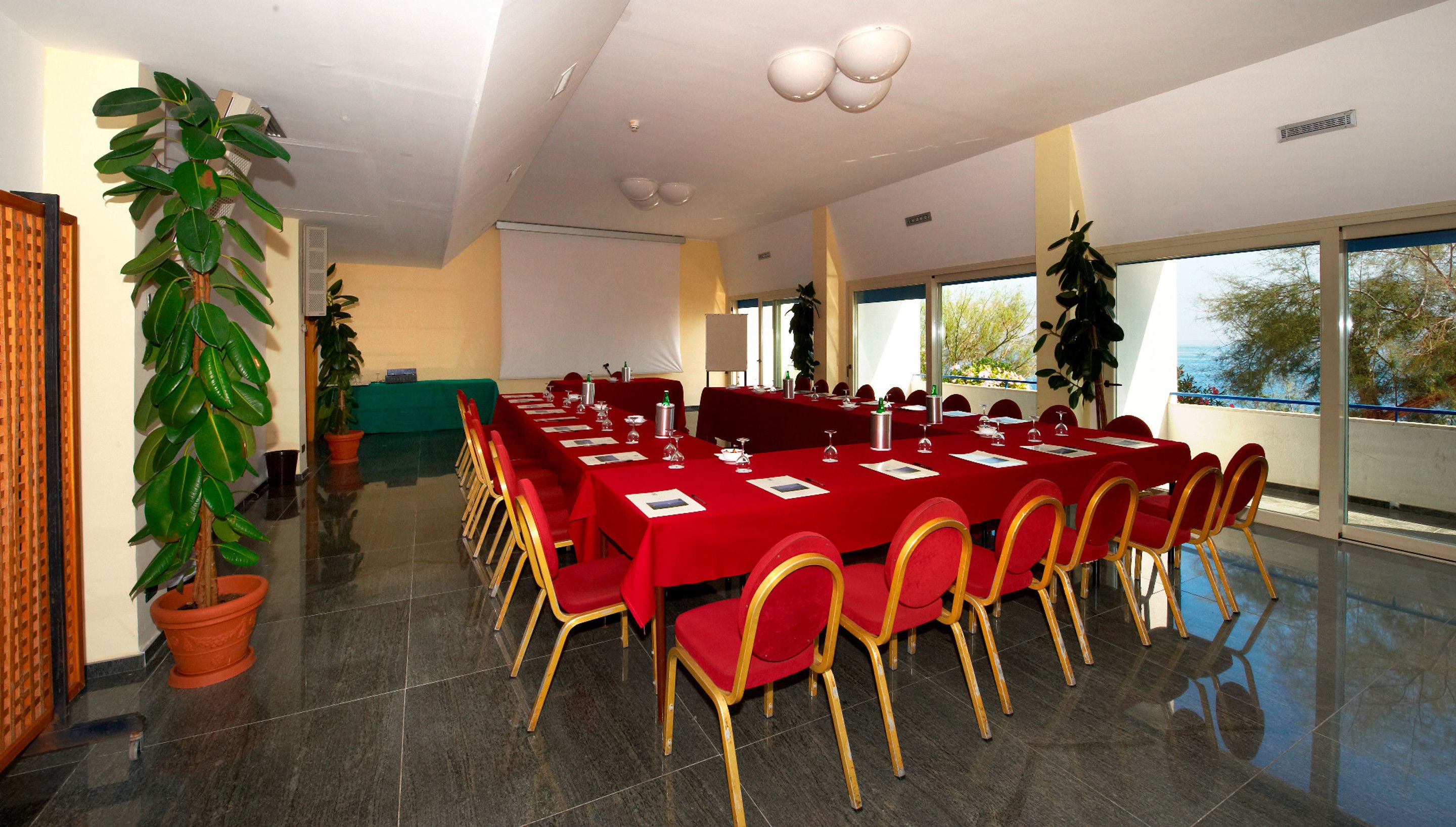 A conference room with a long table, red chairs, and potted plants.