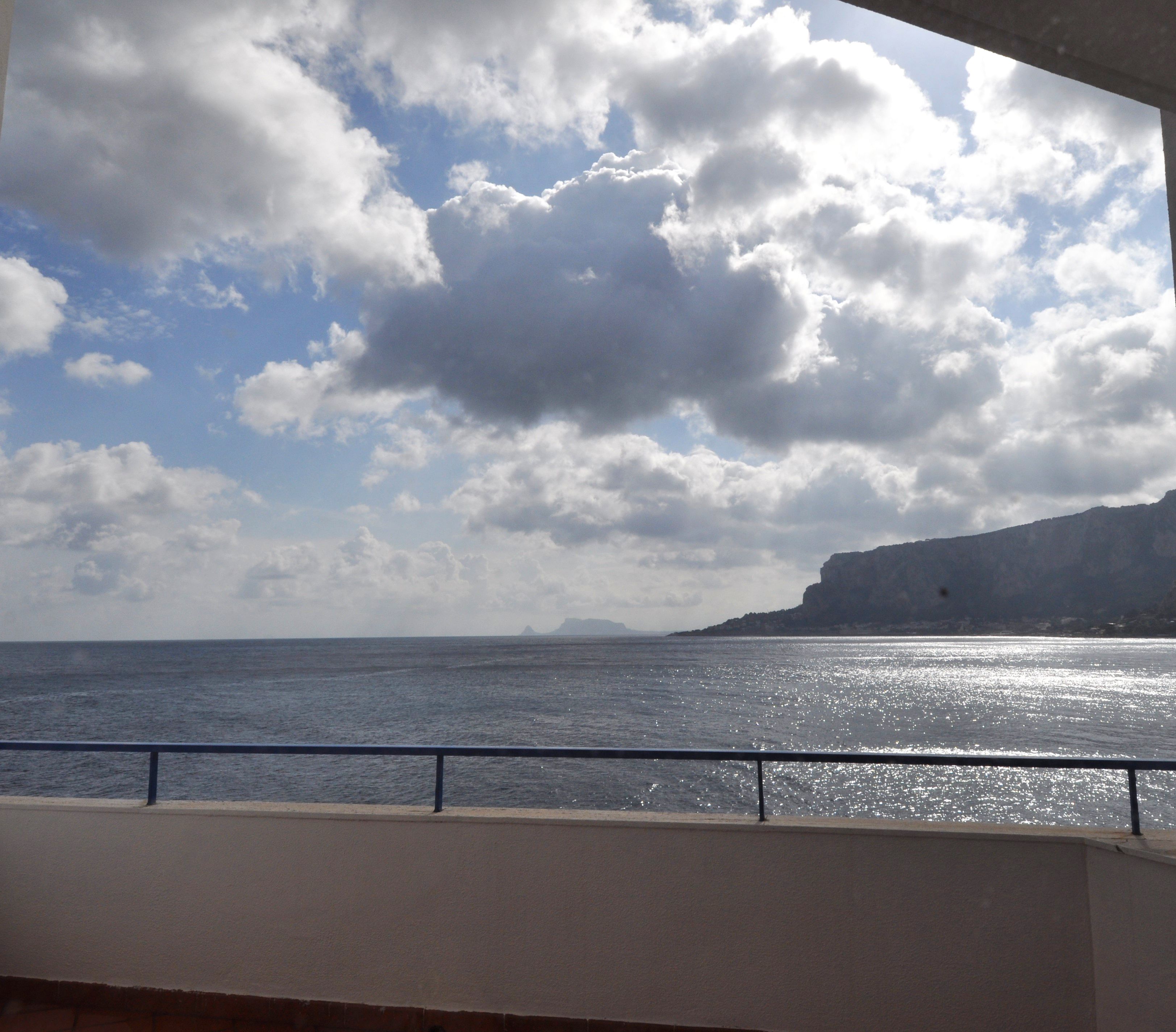 A view of the sea with a railing in the foreground and a rocky cliff in the background.
