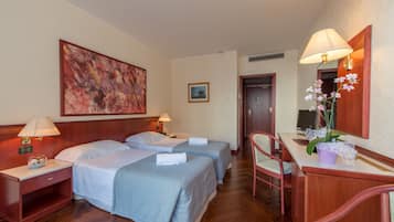 Ein Hotelzimmer mit zwei Betten, einem Schreibtisch, einem Stuhl, einer Lampe und einem Bild an der Wand.