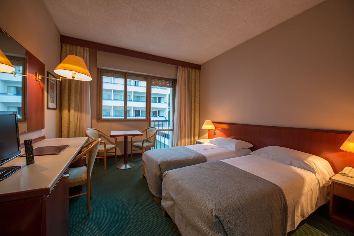 A hotel room with two beds, a desk with a chair, a TV, and a window with curtains.