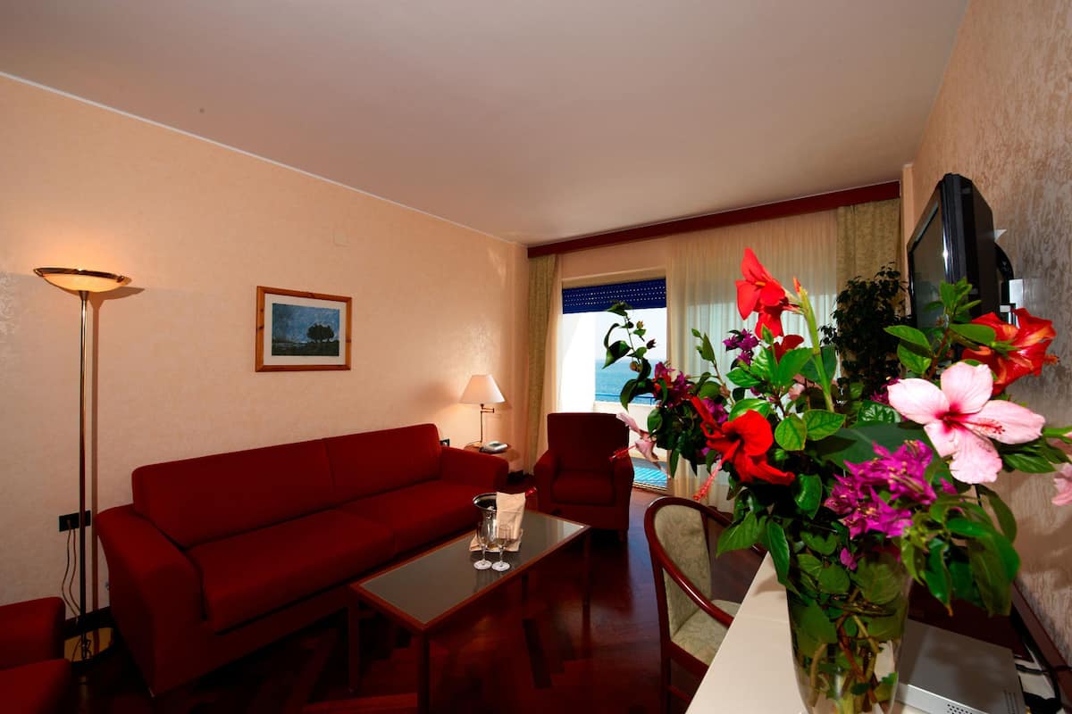 A hotel room with a red sofa, a coffee table, a lamp, a TV, and a large window with curtains.