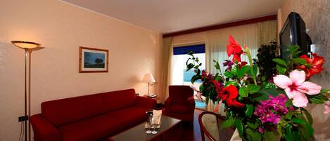 A hotel room with a red sofa, a coffee table, a lamp, a TV, and a large window with curtains.