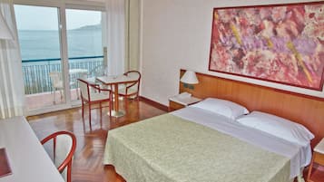 A hotel room with a bed, a desk with a chair, a table, a lamp, and a painting on the wall.