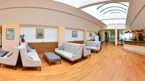 Un hall d’entrée spacieux avec un plafond haut, un plancher en bois et un coin salon agrémenté de canapés et de poufs.