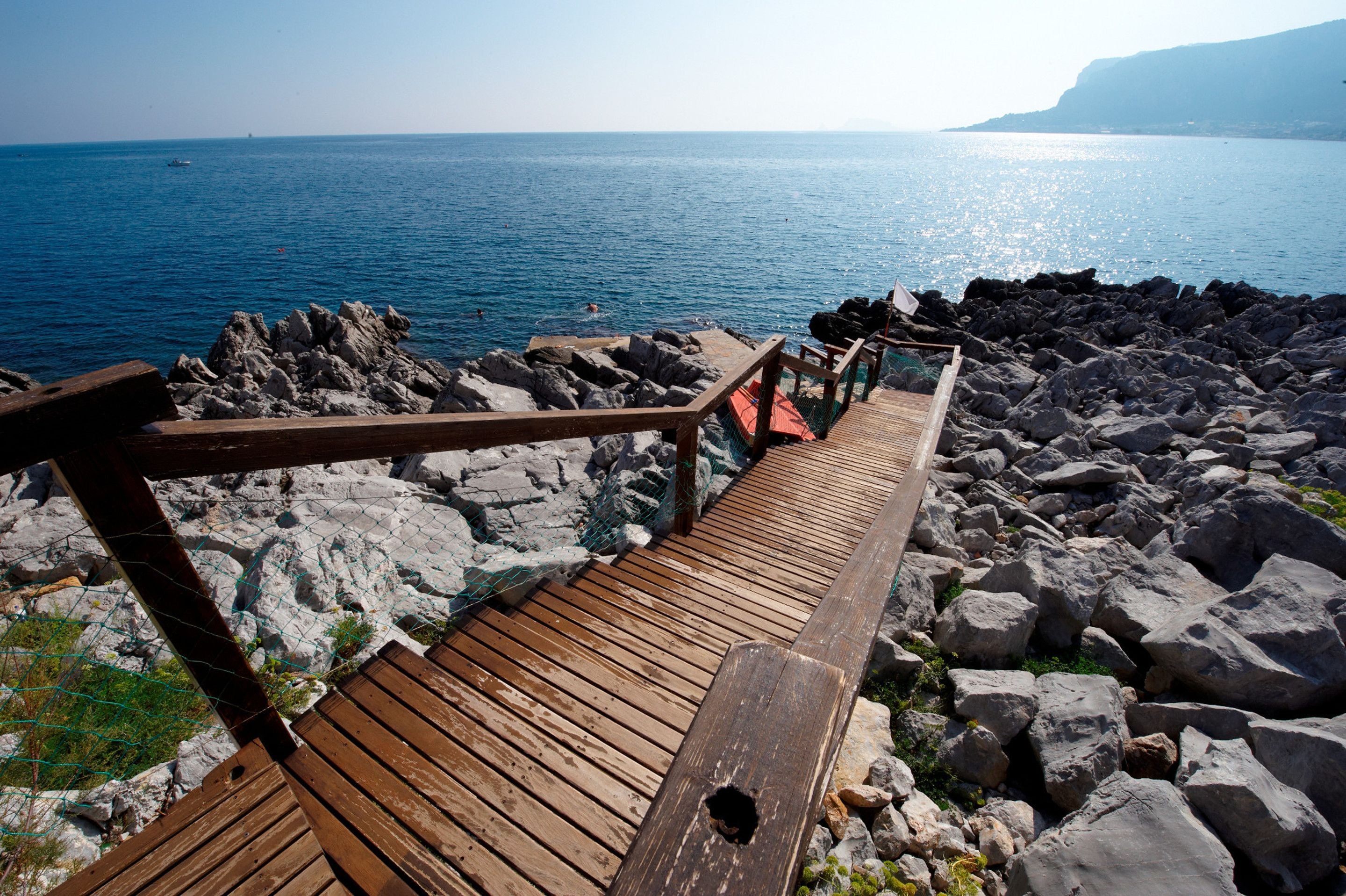 A wooden boardwalk leading to rocky shores with a view of the sea.