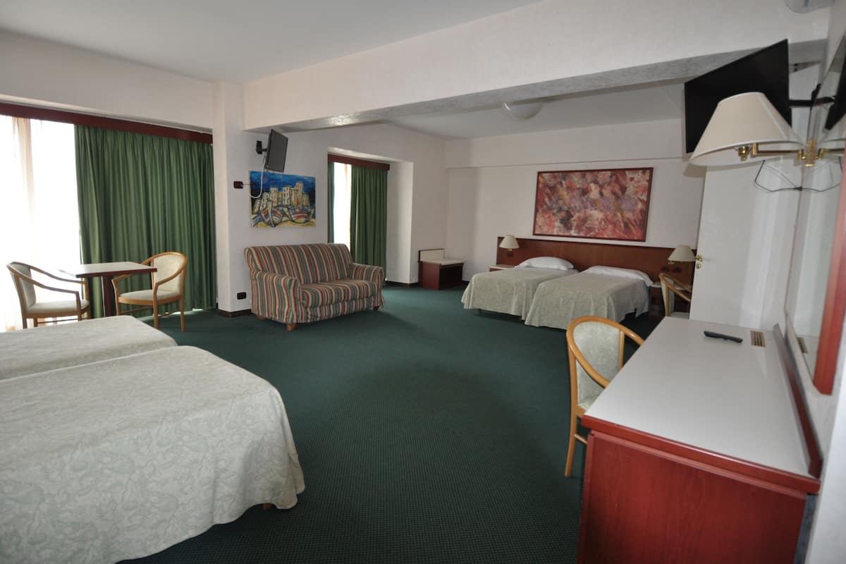 A hotel room with two beds, a desk, a chair, a sofa, and a painting on the wall.