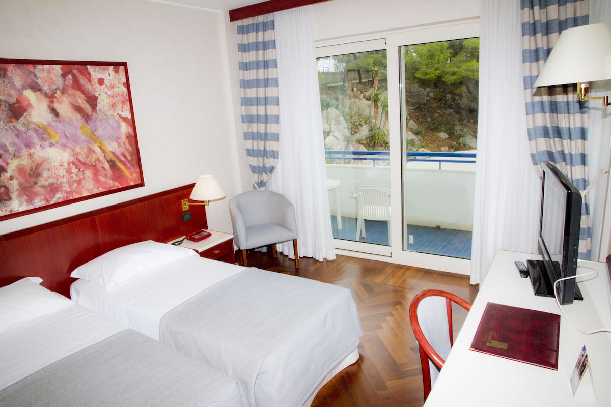 A hotel room with two beds, a desk with a computer, a chair, and a large window with curtains.
